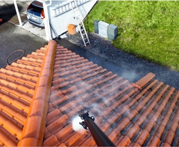 Roof cleaning with a power washer on orange terracotta tiles from a high angle